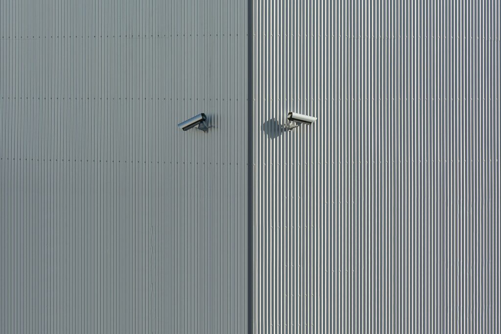 Corrugated metal wall with two mounted security cameras in a minimalist style.