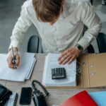 Man in an office reviewing financial papers with a calculator on a desk.