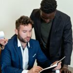 Two businessmen collaborating over a document in a modern office. Professional attire and focused engagement demonstrate teamwork.