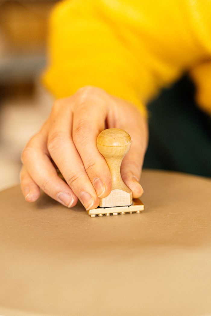 A detailed shot of a hand using a wooden stamp on clay, showcasing craftsmanship.